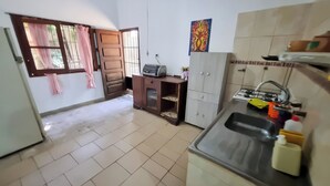 Cocina con lavaplatos, estufa y armarios. Hay una ventana con cortinas y una puerta.