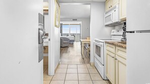 Una cocina moderna con armarios blancos, un microondas y una estufa. Hay un comedor con mesa y sillas, y vistas al exterior a través de una puerta.