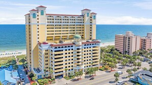 Un hotel de varios pisos con un patio central, vista al mar y zona de estacionamiento.