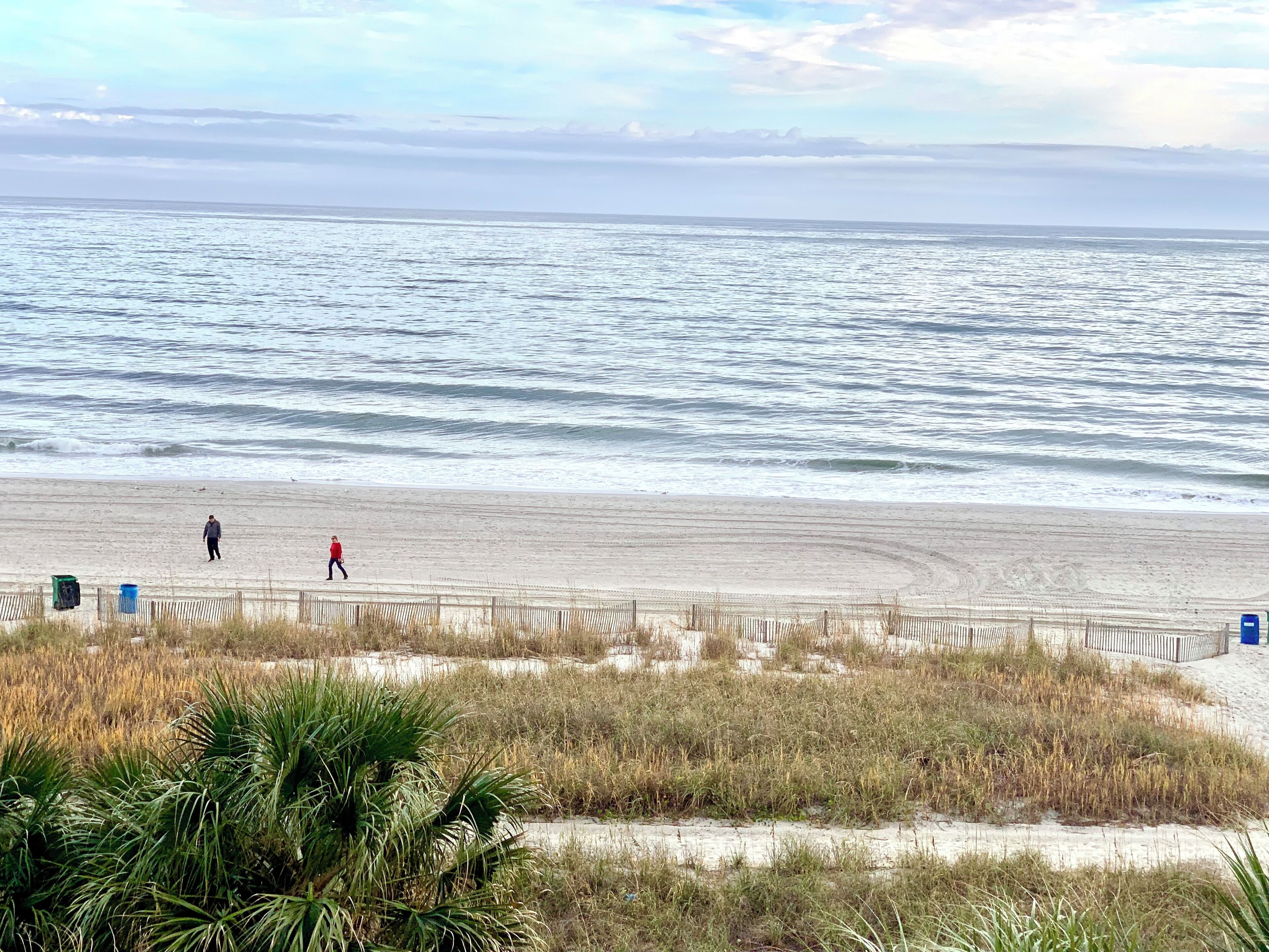 A beach with a sandy shore, a wooden fence, and some vegetation in the foreground.