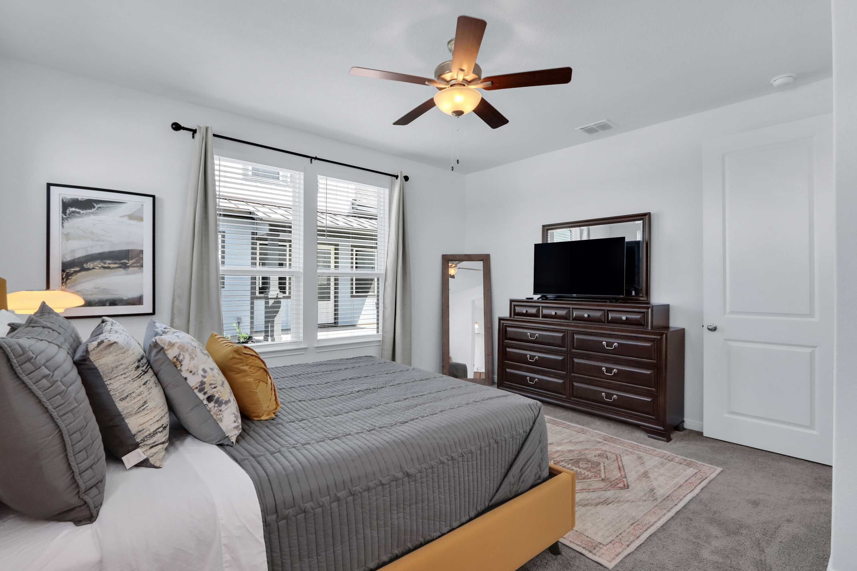 A bedroom with a bed, a dresser, a television, and a ceiling fan.