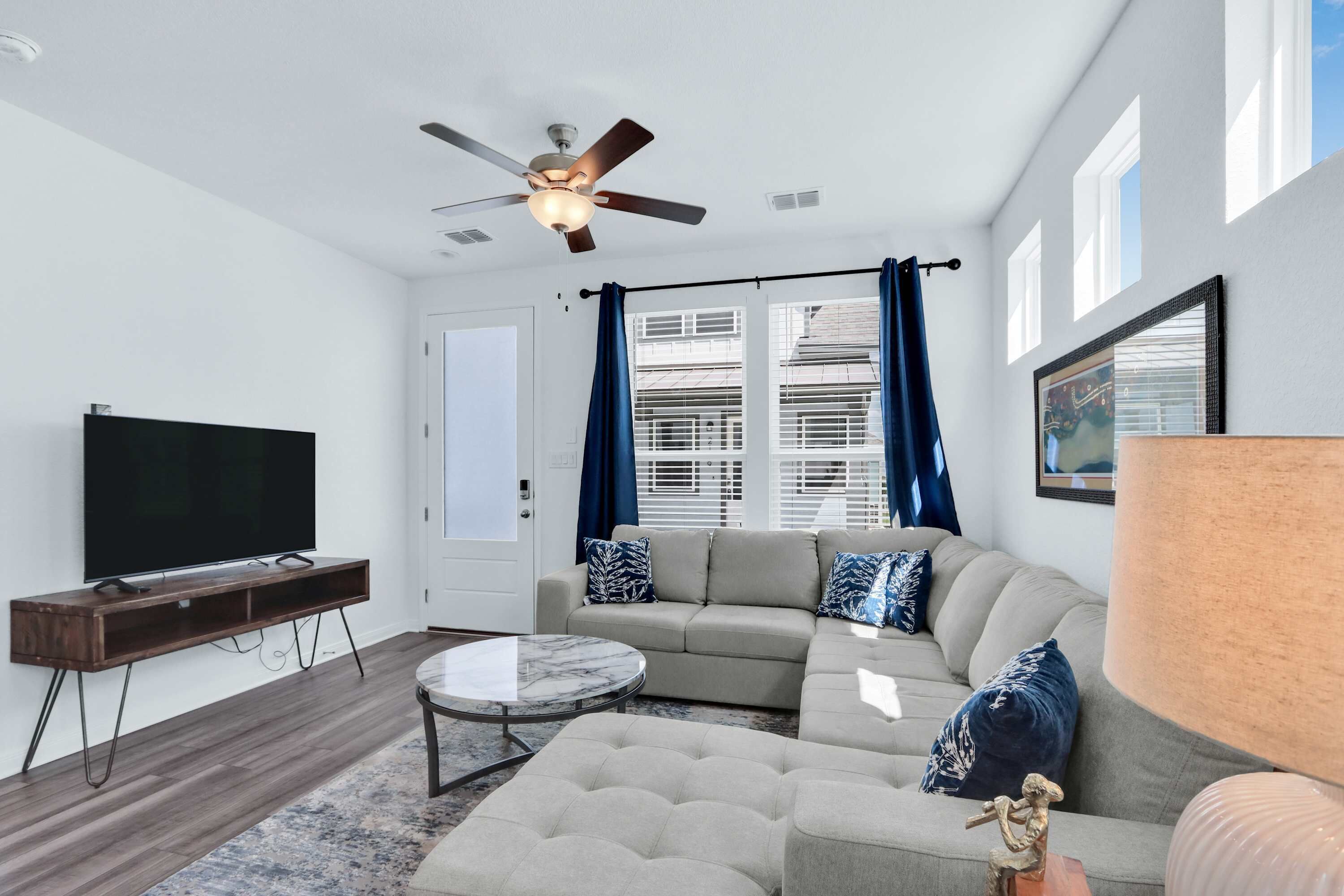 A modern living room with a flat-screen TV, a ceiling fan, a sectional sofa, and a coffee table.