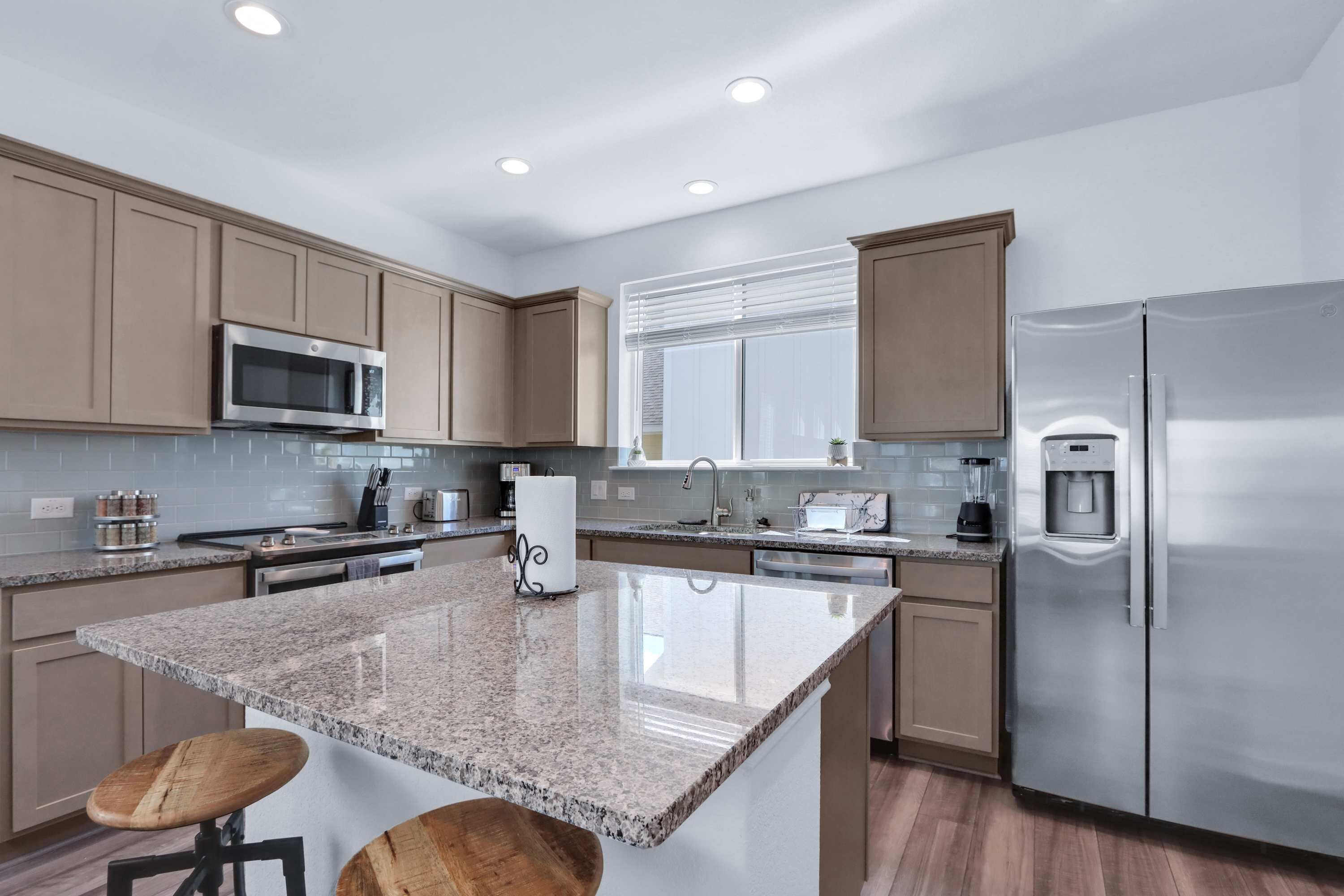 A modern kitchen with granite countertops, stainless steel appliances, and wooden bar stools.