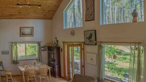 Ein geräumiges Wohnzimmer mit hohen Decken, Holzbalken und großen Fenstern mit Blick auf einen Wald.