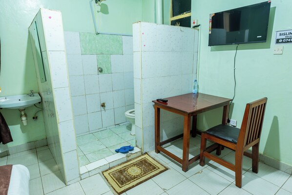 Ein kleines Badezimmer mit Toilette, Waschbecken, Dusche und einem Tisch mit Stuhl.