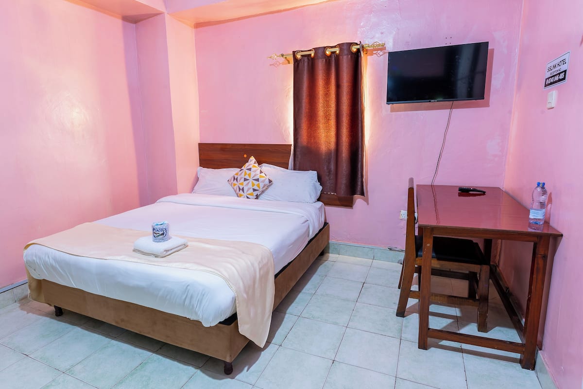 A bedroom with a bed, a television mounted on the wall, a desk, and a chair.