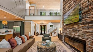 A spacious living area with a stone fireplace, a high ceiling, and a second-floor balcony.