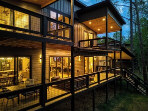Une cabane en bois à plusieurs niveaux, comprenant un coin repas, une cheminée et un escalier menant à une terrasse supérieure.