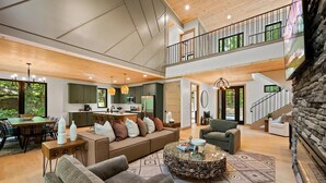 A spacious living area with a high ceiling, a kitchen, a dining area, and a staircase leading to an upper level.