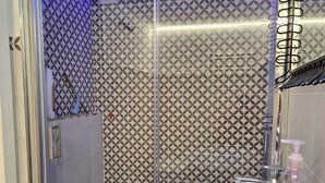 A modern bathroom with a glass shower enclosure, patterned tiles, and a white sink with a soap dispenser.