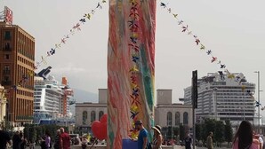 A large cylindrical structure with colorful floral patterns, surrounded by a crowd of people and buildings in the background.