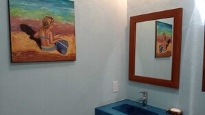 A bathroom with a blue sink, a painting of a person on a beach, and a mirror.