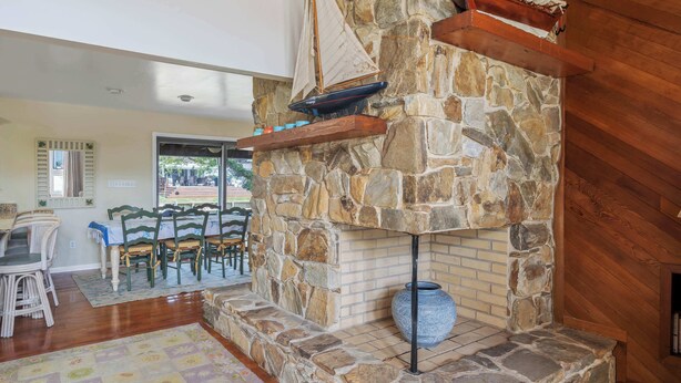 Una chimenea de piedra con un jarrón azul, estantes de madera y un comedor con sillas de mimbre.