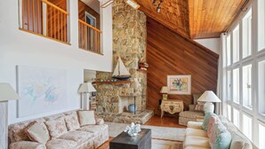 Un salón espacioso con chimenea de piedra, vigas de madera y ventanas amplias.