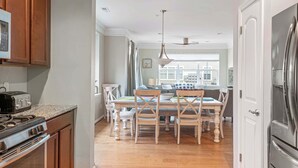 Une cuisine avec des meubles en bois, un réfrigérateur en acier inoxydable, une table à manger avec des chaises et un ventilateur de plafond.