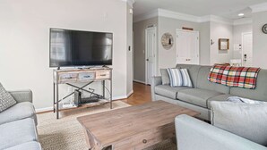Un salon équipé d’un téléviseur à écran plat, d’une table basse en bois et d’un canapé gris recouvert d’un plaid.