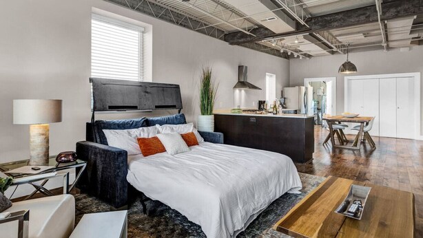 Een moderne slaapkamer met een bed, nachtkastjes, een bureau en een kitchenette.