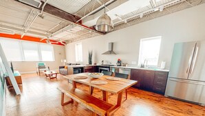 Een ruime keuken met een houten tafel en bank, een roestvrijstalen koelkast en een groot raam dat natuurlijk licht binnenlaat.