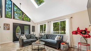 A modern living room with a sectional sofa, a coffee table, and large windows offering a view of trees.