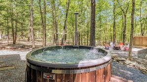 A hot tub in a forested area with a wooden deck and outdoor seating.