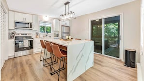 A modern kitchen with a central island, bar stools, and a large window.