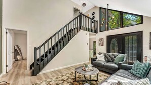 Una sala de estar moderna con una escalera, un sofá, una mesa de centro y ventanas amplias.