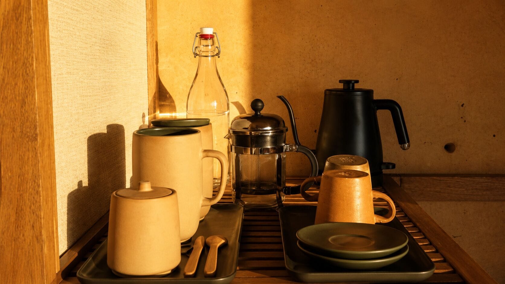 A kitchenette with a coffee maker, a kettle, a bottle, and various mugs and cups.
