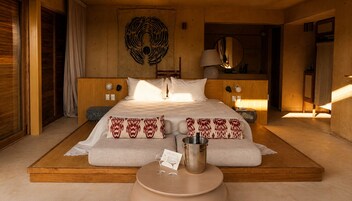 Un dormitorio espacioso con una cama grande, una mesita de noche con lámpara y un espejo en la pared.