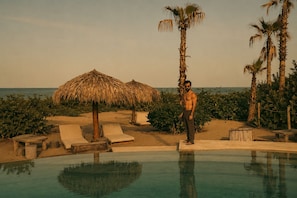 A man standing by a pool with lounge chairs and palm trees. - KYMAIA Hotel Puerto Escondido (Santa Maria Colotepec)