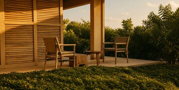 Un espacio al aire libre con dos sillas de madera y una pequeña mesa, rodeado de follaje y una estructura de madera.
