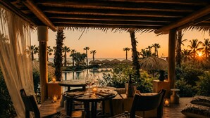 Un espace extérieur aménagé pour prendre les repas, avec vue sur l’océan et les palmiers au coucher du soleil.