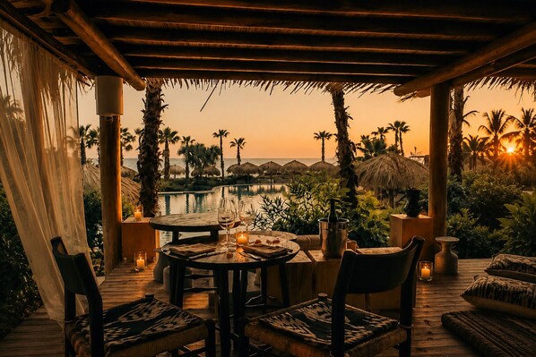 An outdoor dining area with a view of the ocean and palm trees at sunset. - Hotel Kymaia, WorldHotels Crafted (Santa Maria Colotepec)