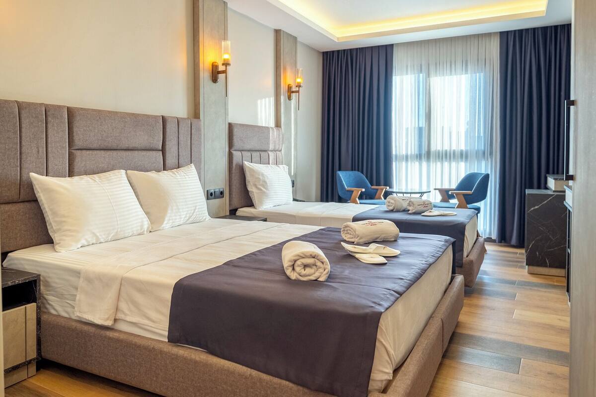 Quarto de hotel moderno com uma cama grande, mesas de cabeceira, uma escrivaninha e um espaço de estar com cadeiras.