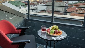 A balcony with a red chair, a table with fruits and a drink, and a sunset view.