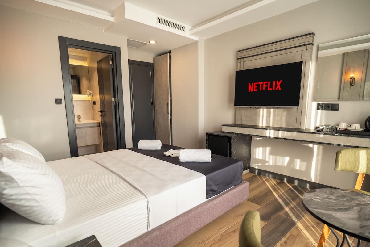 Quarto de hotel com cama, escrivaninha, cadeira, televisão e banheiro.