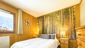 A bedroom with a large bed, wooden walls, a window with curtains, a wall-mounted lamp, and a dresser. - Apartment with mountain view in Saint-Gervais (Saint-Gervais-les-Bains)