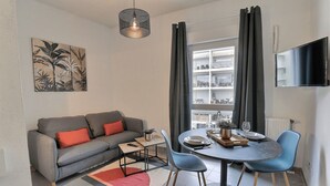 A modern living room with a grey sofa, a coffee table, and a dining area with blue chairs. - Lovely apartment for 2 in Marseille (Marseille)