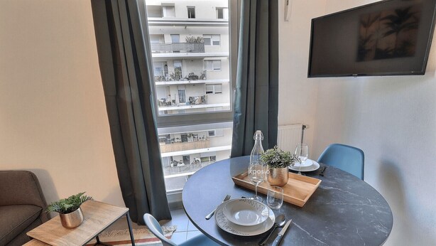 A modern dining area with a round table set for two, a small potted plant, and a remote control on a side table. - Lovely apartment for 2 in Marseille (Marseille)