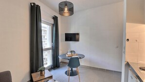 A modern living room with a round dining table, a sofa, a TV mounted on the wall, and a window with curtains. - Lovely apartment for 2 in Marseille (Marseille)