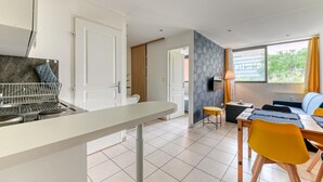 A modern kitchen with a white countertop and a built-in oven. There is a dining area with a table and chairs, and a sofa. - Apartment - 4P -  Villeurbanne (Villeurbanne)