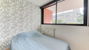 A room with a bed, a window with a view of buildings, and a patterned wallpaper. - Apartment - 4P -  Villeurbanne (Villeurbanne)