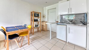 A compact kitchen with white cabinets, a built-in microwave, and a sink. There is a small dining table with chairs and a shelf with kitchen appliances. - Apartment - 4P -  Villeurbanne (Villeurbanne)