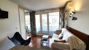A room with a sofa, a chair, a small table, and a TV mounted on the wall. - Charming apartment 20 m from the beach in Arcachon (Arcachon)