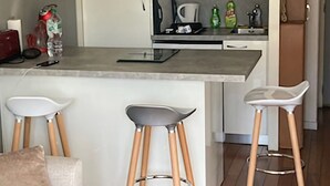 A compact kitchen with a central island, two bar stools, and a sofa in a modern apartment. - Charming apartment 20 m from the beach in Arcachon (Arcachon)