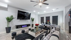 Un salon moderne doté d’un téléviseur à écran plat, d’un ventilateur de plafond et d’un canapé d’angle.