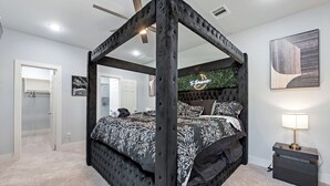 Un lit à baldaquin à quatre poteaux avec une tête de lit capitonnée, une table de chevet avec une lampe et une œuvre d’art accrochée au mur.