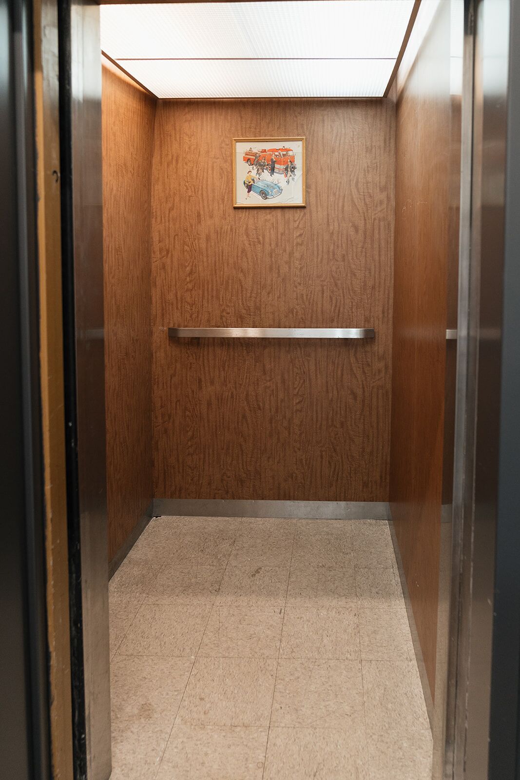 Un ascensor con pared de madera, barandilla de metal y un cuadro enmarcado de bomberos.