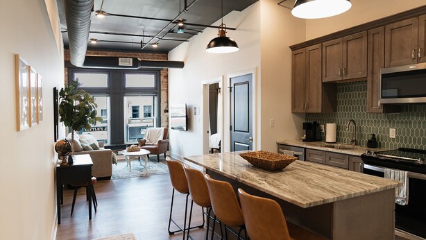 A modern kitchen with a large island, bar stools, and a dining area with a sofa and coffee table.