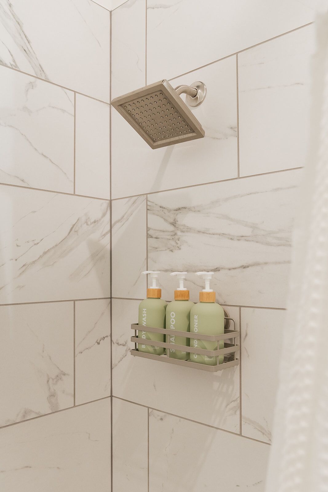 A bathroom with a shower, marble tiles, and a soap dispenser shelf.