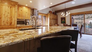A kitchen with wooden cabinets, granite countertops, and a dining area with chairs and a table. - PG305 Beautiful Copper Getaway! (Frisco)